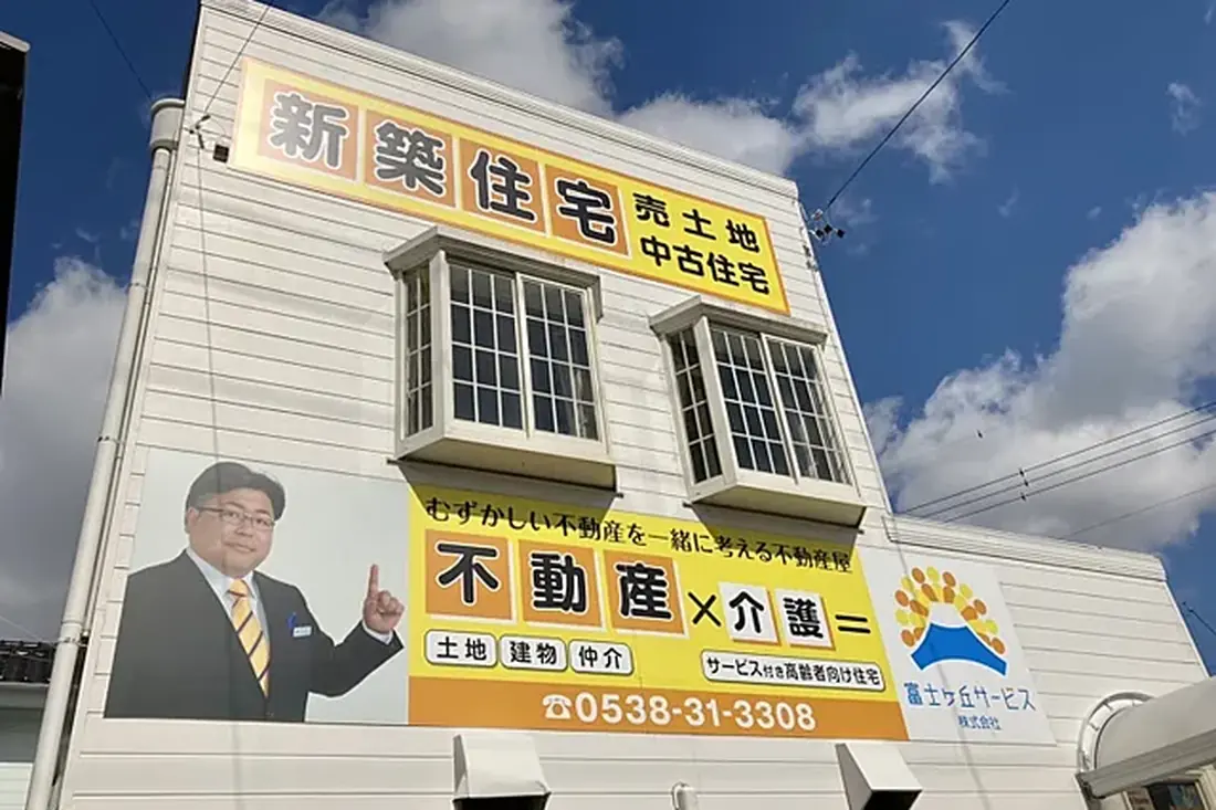 富士ヶ丘サービスの看板。「むずかしい不動産を一緒に考える不動産屋 不動産×介護＝」と代表の写真、電話番号0538-31-3308